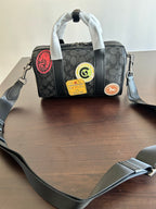 Coah bag with crossbody strap, black patterned exterior and front circular badge patches