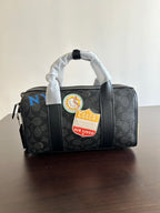 Coah bag front view with two handles and zipper, black patterned fabric with badge patches