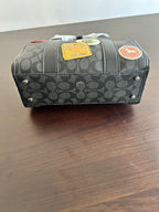 Coah bag side profile with zipper, black patterned body and stitched emblem patch detail