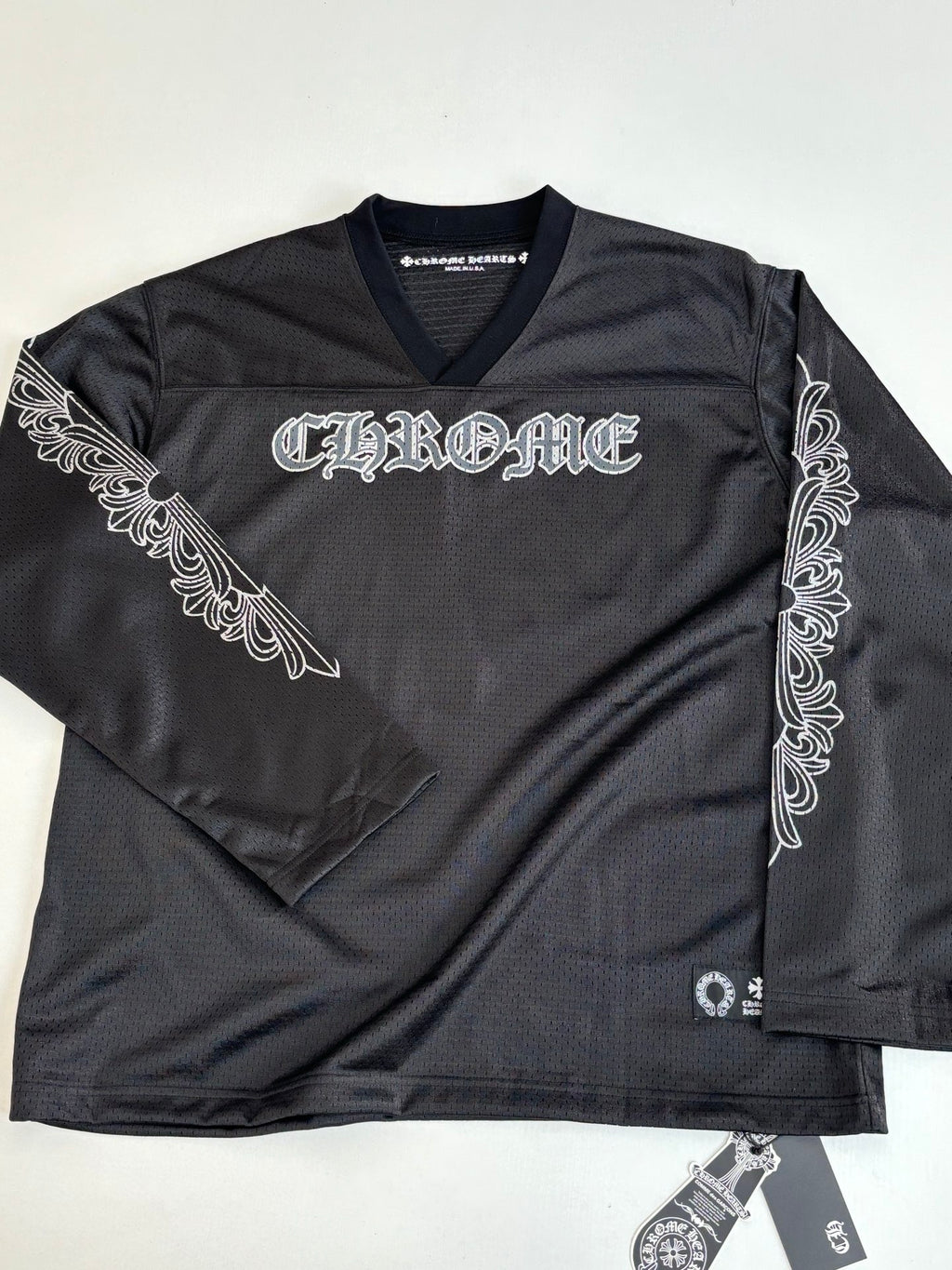 Black long-sleeve top with V-neck and ornate logo embroidery on chest.