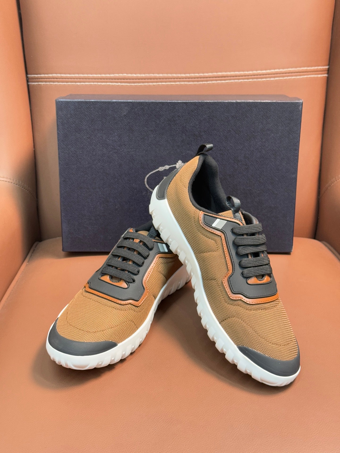 Pair of tan lace-up sneakers with black laces, orange trim, and white cushioned sole