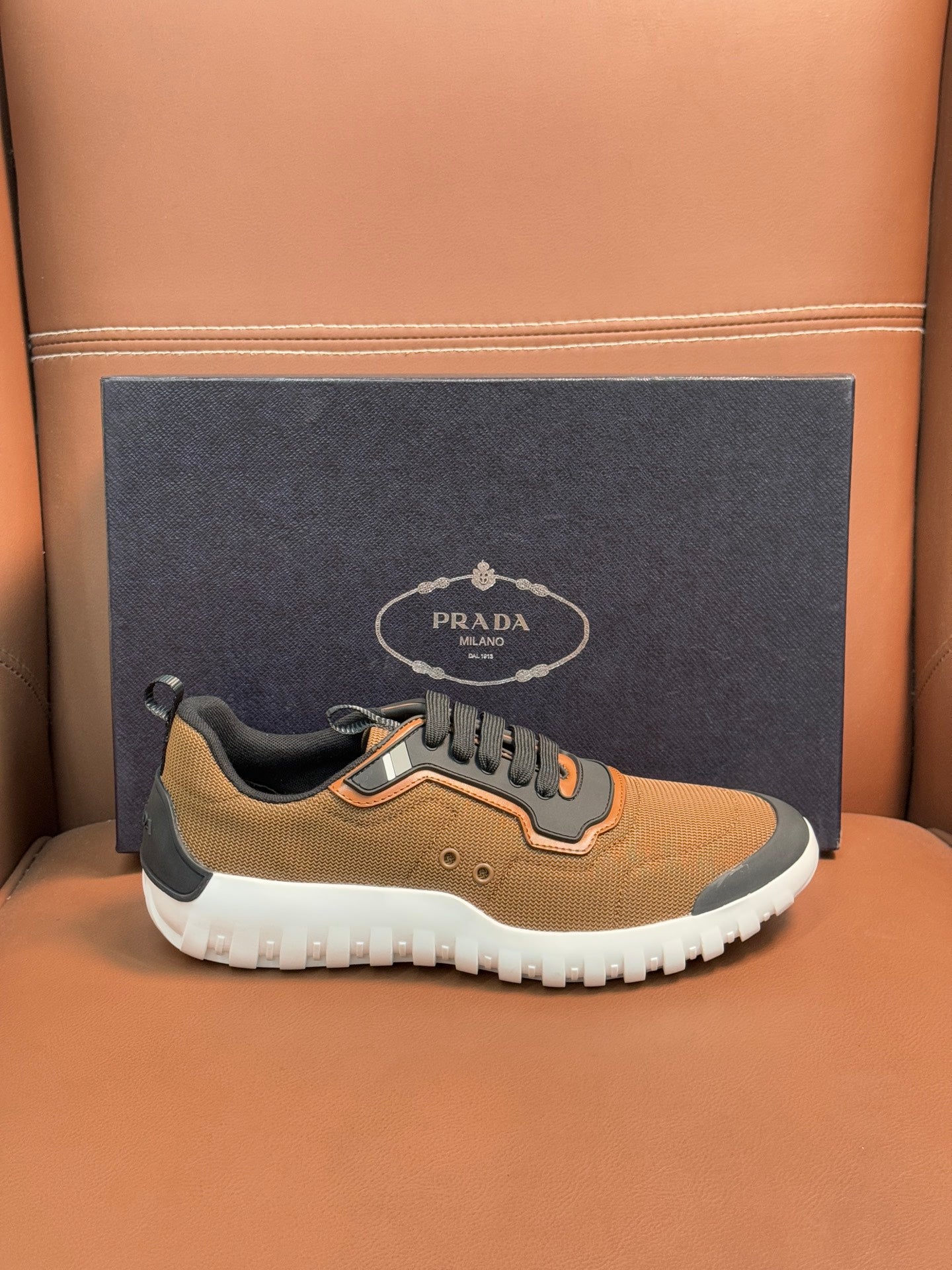 Tan and black lace-up sneakers with orange trim and white outsole, Prada emblem on side