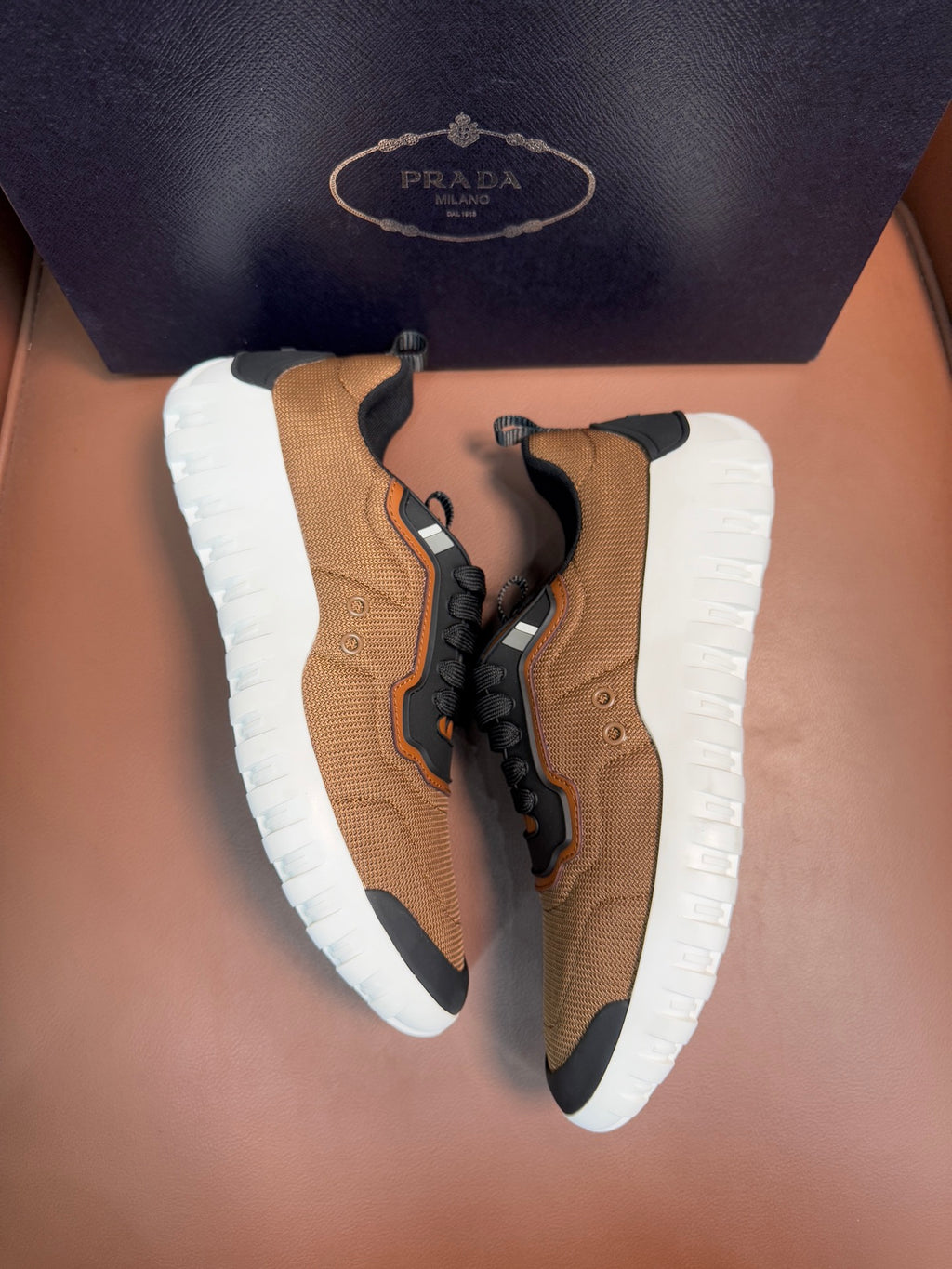 Tan and black lace-up sneakers with orange accents and white rubber soles, Prada details