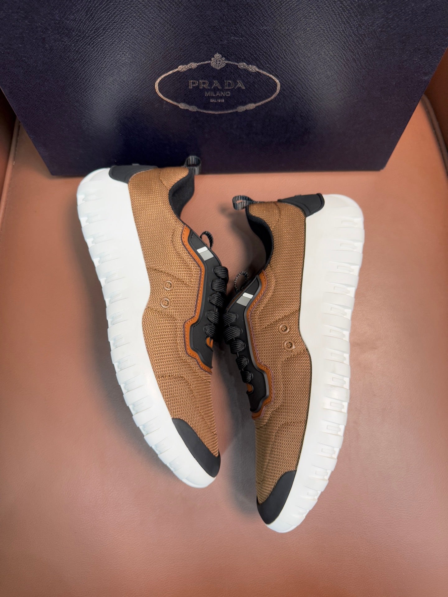 Tan and black lace-up sneakers with orange accents and white rubber soles, Prada details