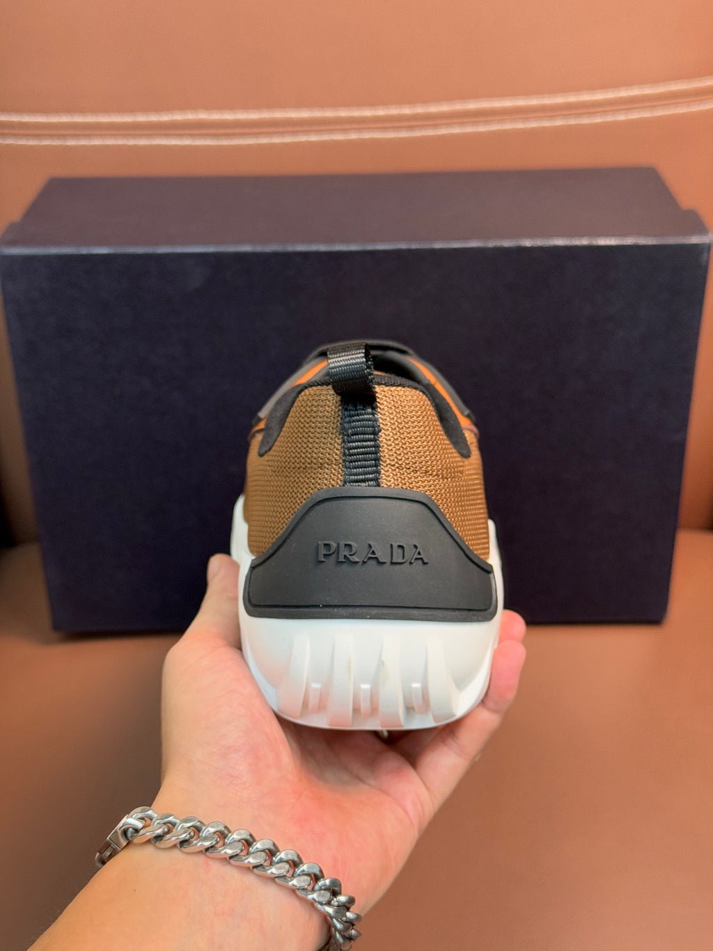 Back view of tan sneaker with black heel pull and Prada logo on white outsole