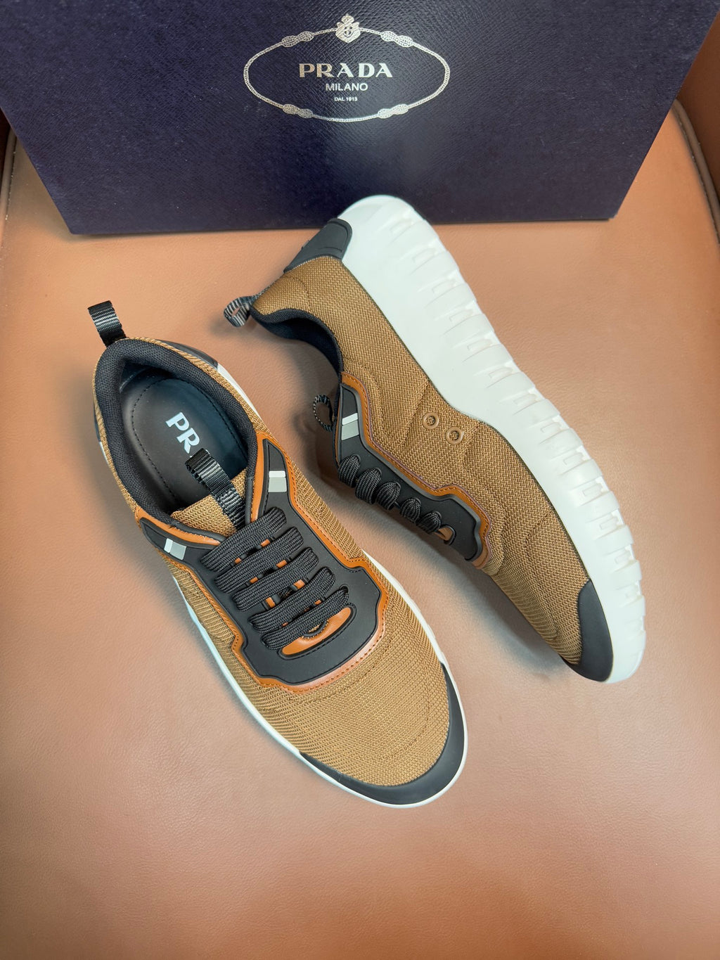 Tan and black lace-up sneakers with orange trim, thick white outsole, Prada logo tab