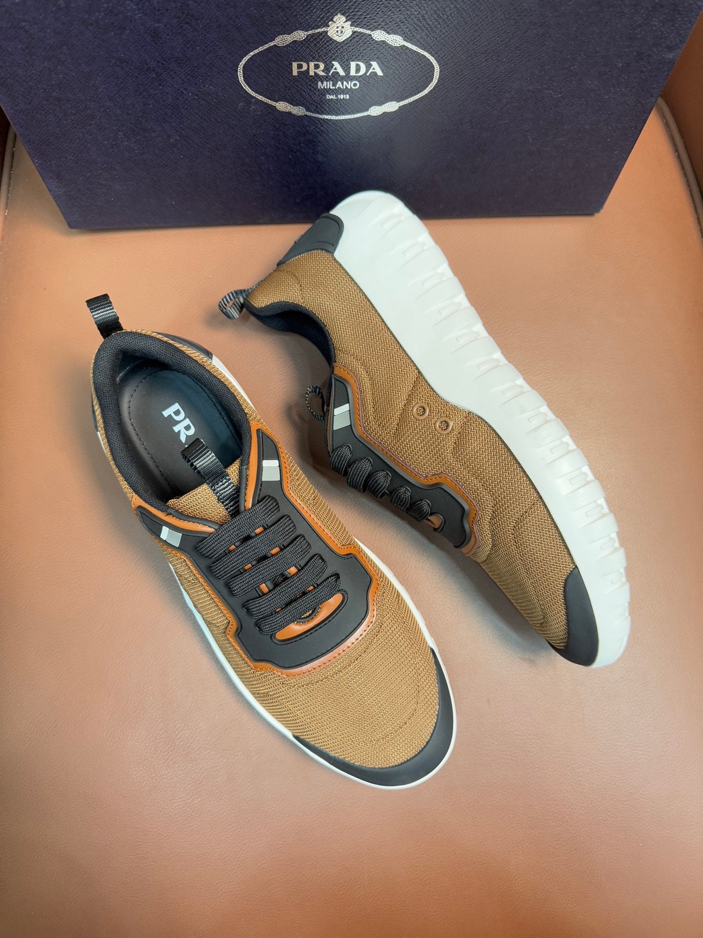 Tan and black lace-up sneakers with orange trim, thick white outsole, Prada logo tab