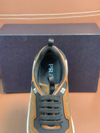 Front view of tan lace-up sneaker with black laces, orange trim, and Prada logo patch
