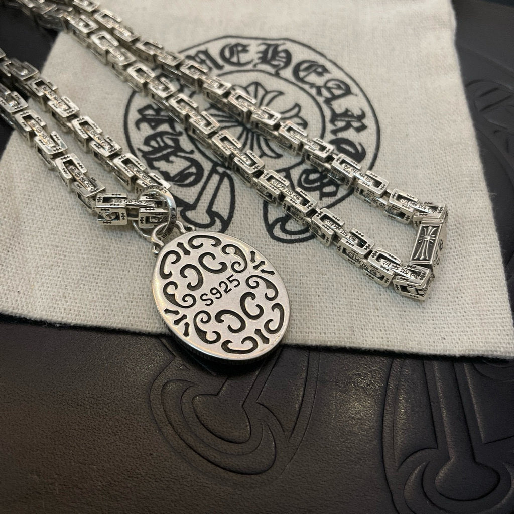 Silver-tone oval medallion pendant on chain necklace, close-up on cloth and box.