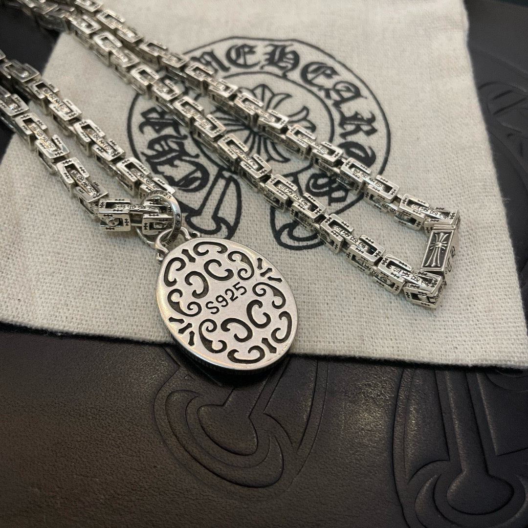 Silver-tone oval medallion pendant on chain necklace, close-up on cloth and box.