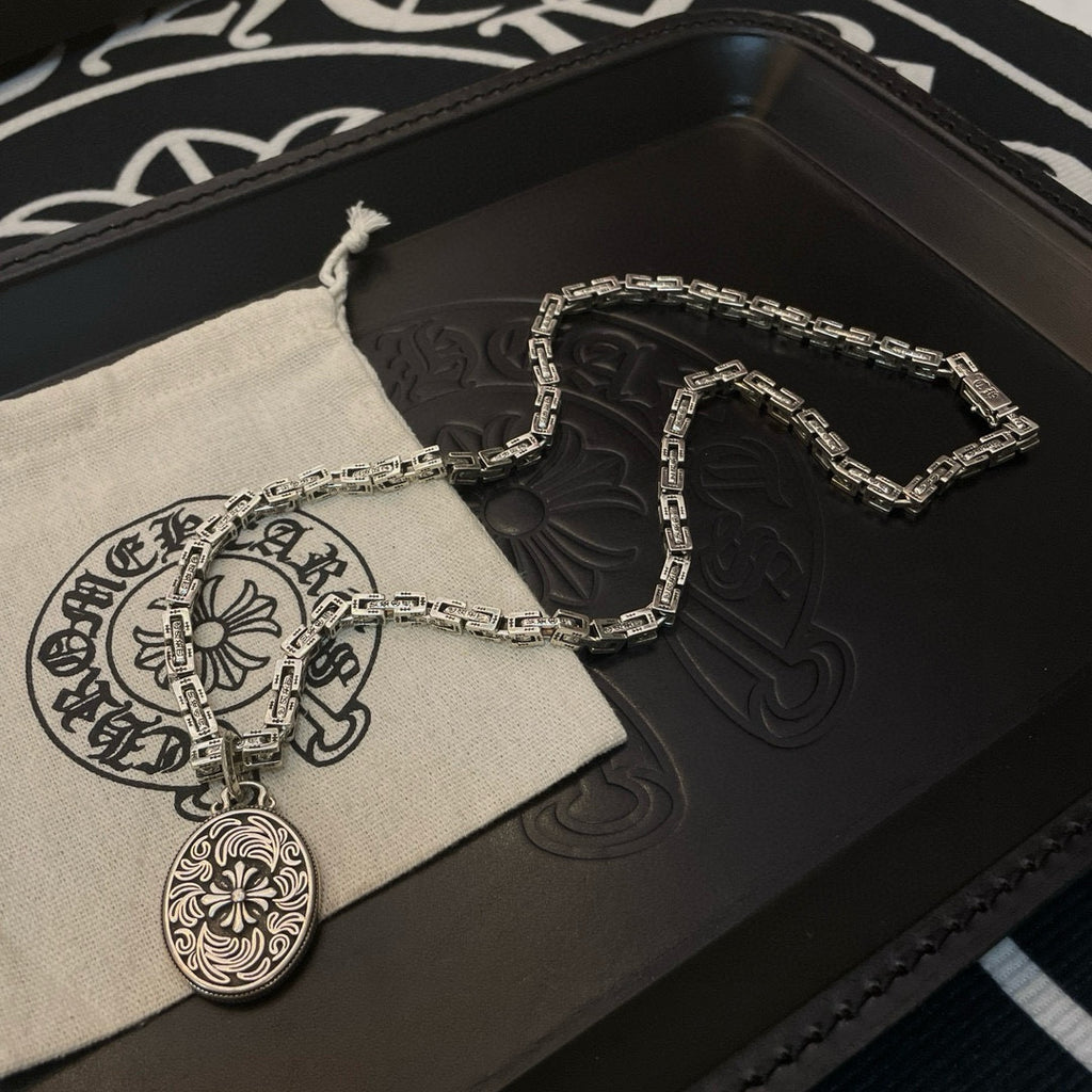 Silver-tone chain necklace with oval medallion pendant and fabric pouch on black box.