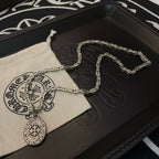 Silver-tone chain necklace with oval medallion pendant and fabric pouch on black box.