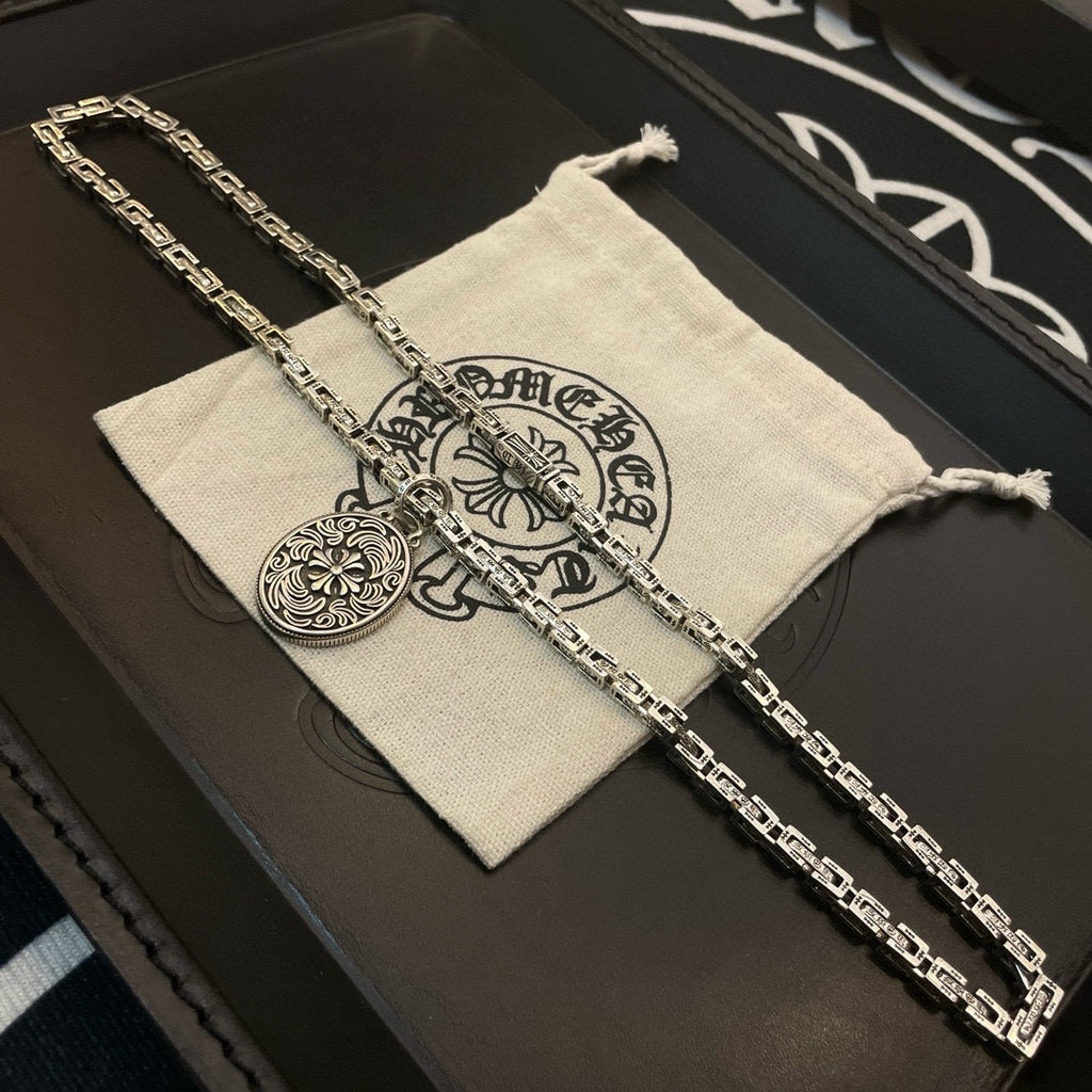 Silver-tone chain necklace with oval medallion pendant with fabric pouch, flat lay.