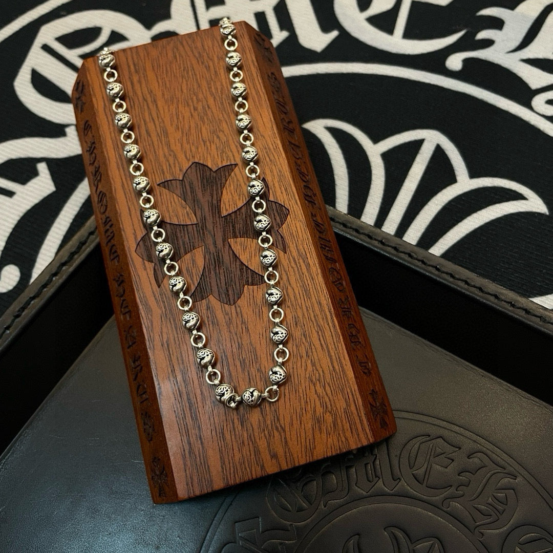 Silver ball chain necklace laid over a wooden charm card with cutout emblem.