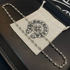 Silver ball chain necklace resting on a black box with a light drawstring bag.