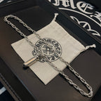 Chrome chain necklace with capsule pendant, laid across a fabric pouch
