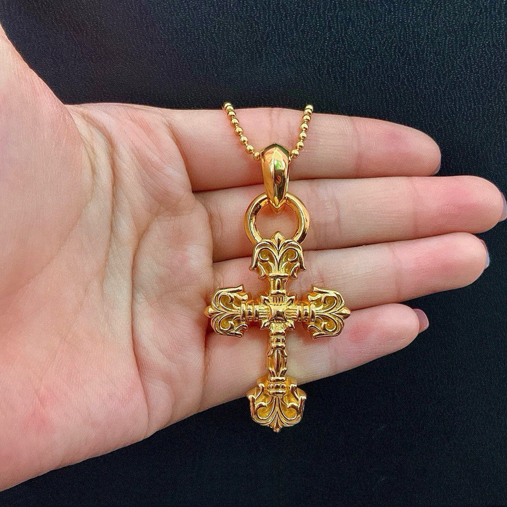 Gold tone cross pendant necklace held in palm on a beaded chain