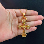 Gold tone cross pendant necklace held in palm on a beaded chain