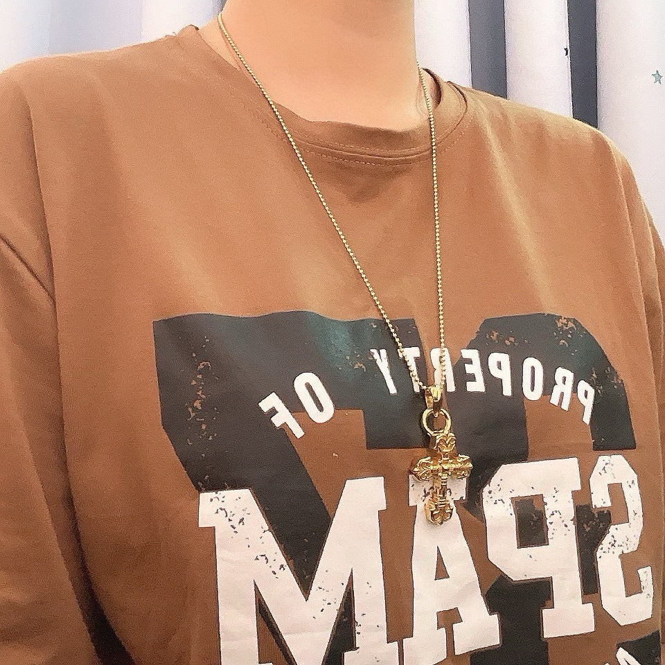 Gold tone cross pendant necklace worn over a graphic T-shirt