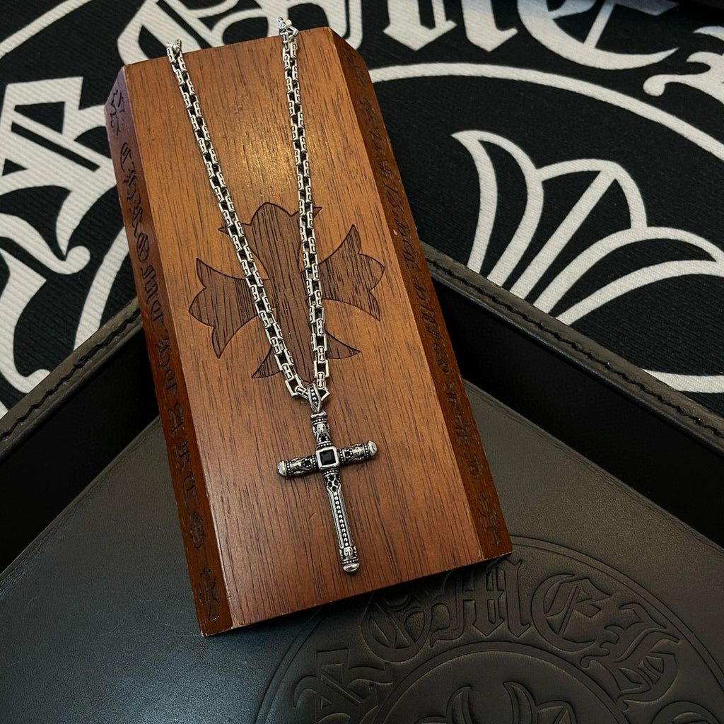Silver-tone cross pendant necklace on wooden display stand over black box.