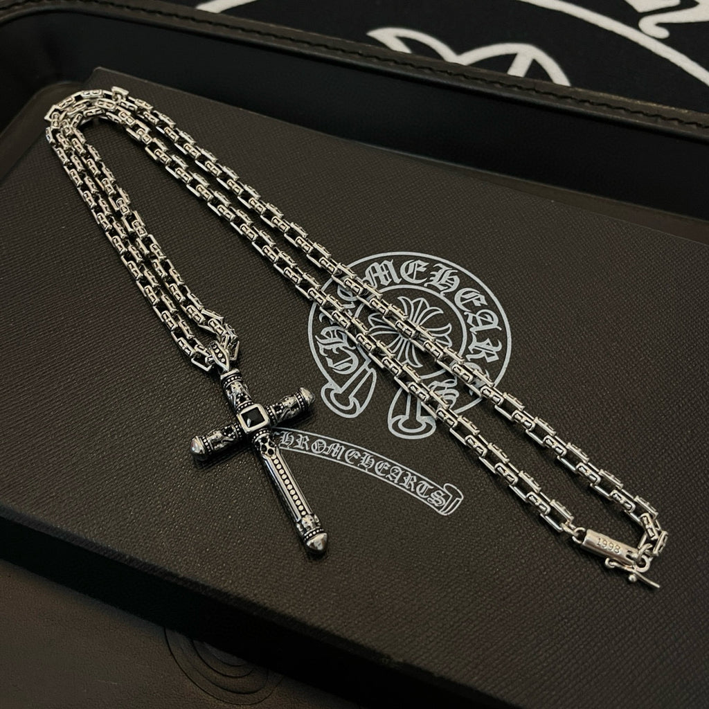Silver-tone cross pendant necklaces with chain links on black gift box surface.