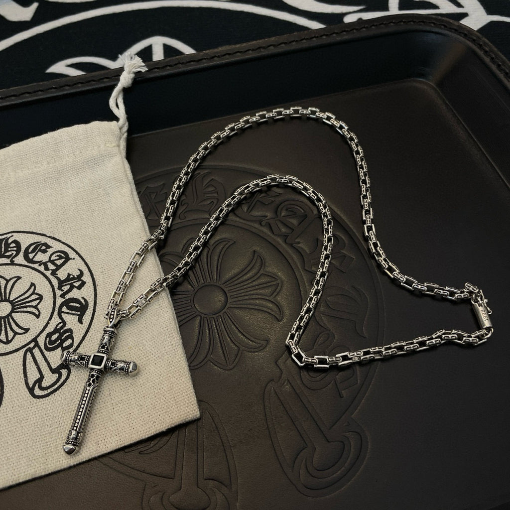 Silver-tone cross pendant necklace draped on beige drawstring pouch over black box.