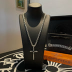 Silver cross pendant necklace on black bust display with layered chain links.