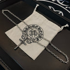 Silver-tone cross pendant necklace with chain links inside beige drawstring pouch.