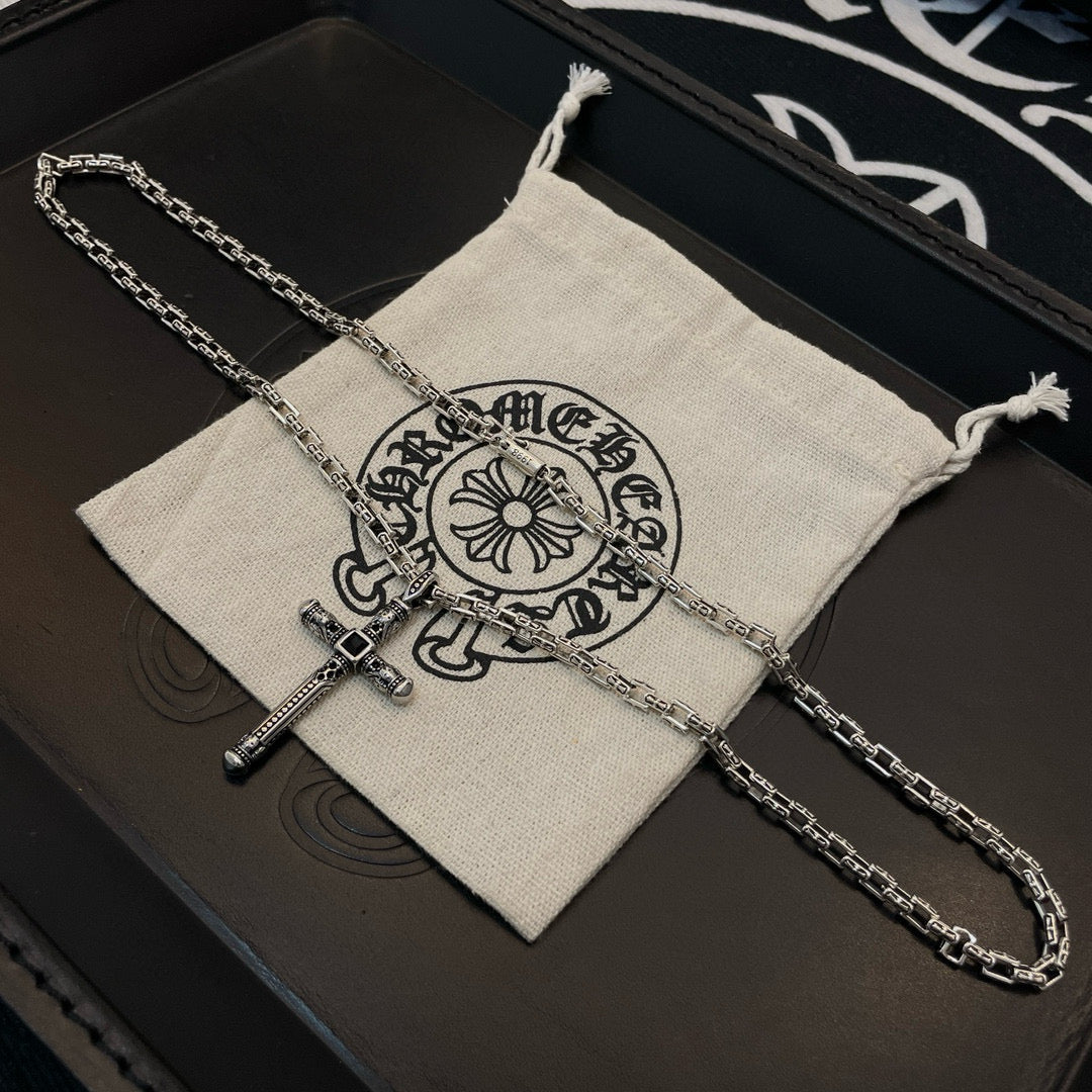 Silver-tone cross pendant necklace with chain links inside beige drawstring pouch.