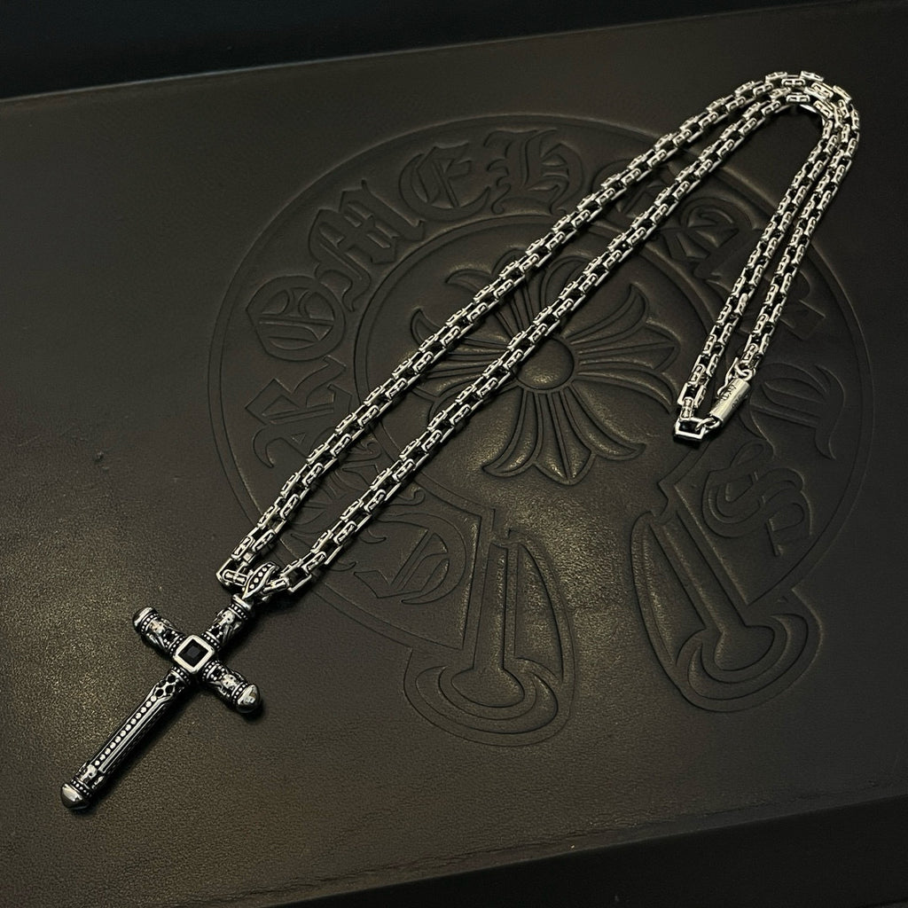 Silver-tone cross pendant necklace with chain links on embossed black box.