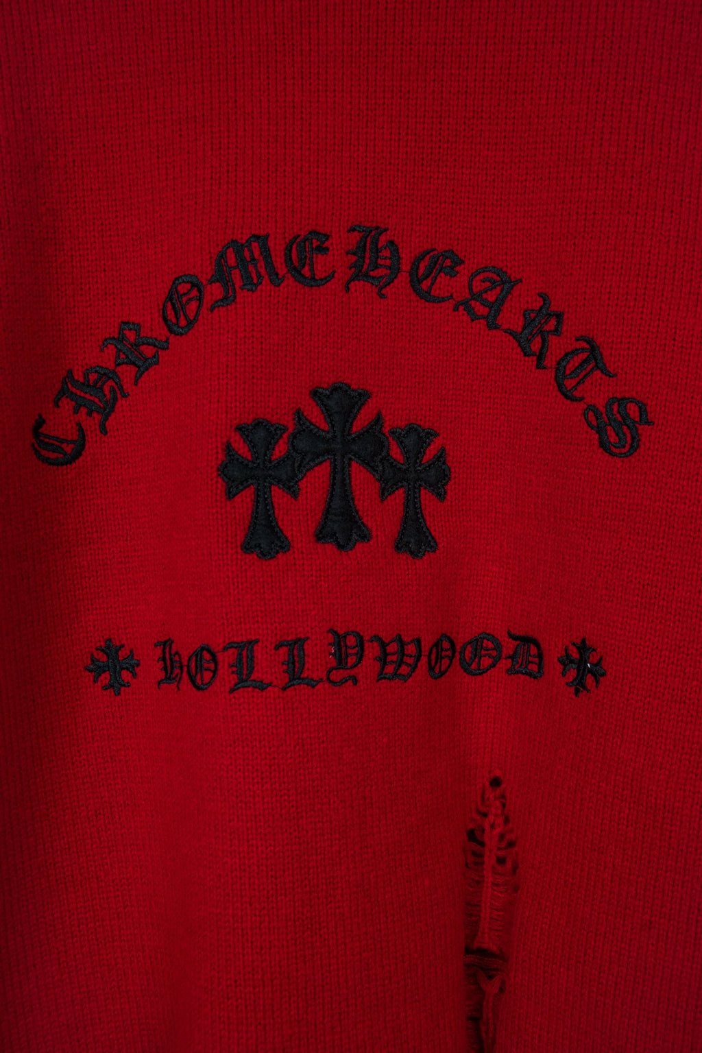 Red sweater with black arched lettering and cross-shaped embroidery