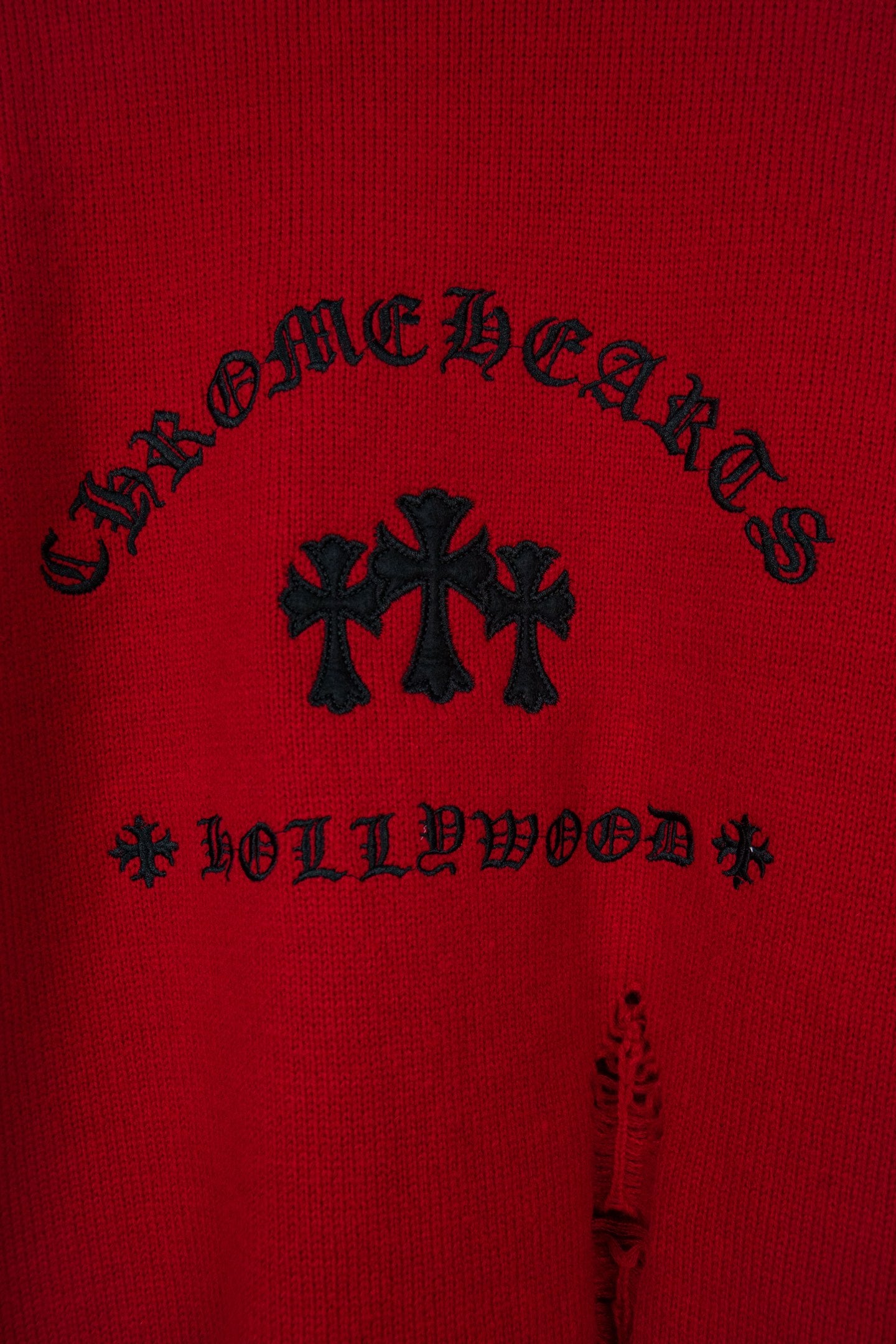 Red sweater with black arched lettering and cross-shaped embroidery