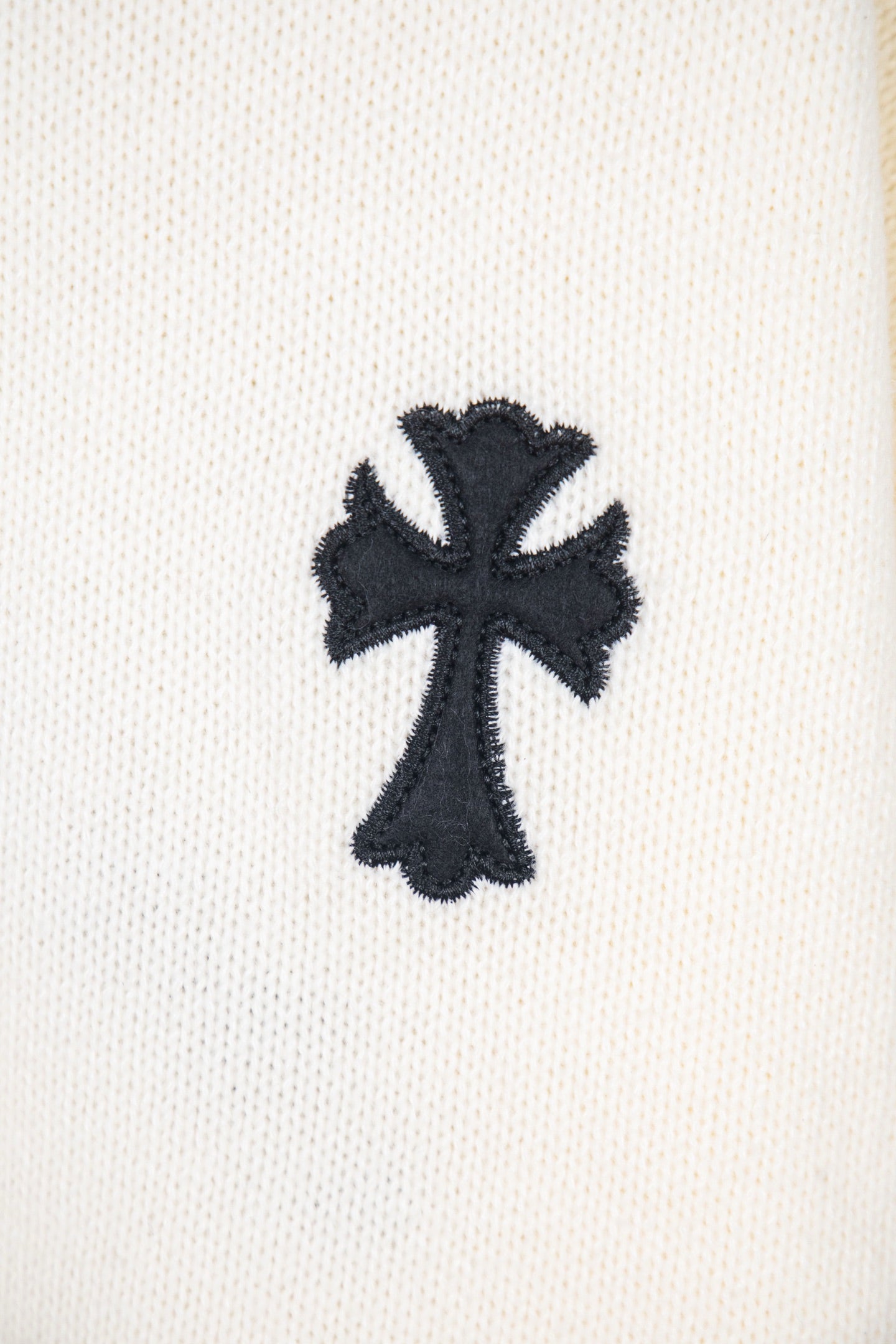 Cream sweater sleeve with black cross appliqué