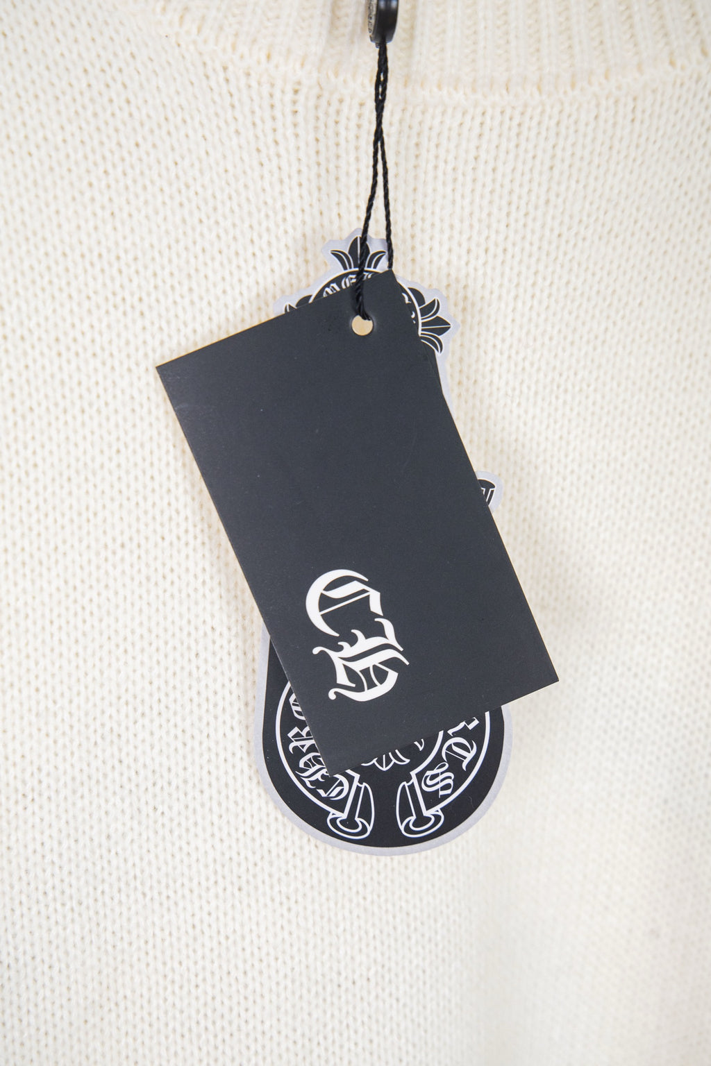 Cream knit sweater close-up with black logo hang tag
