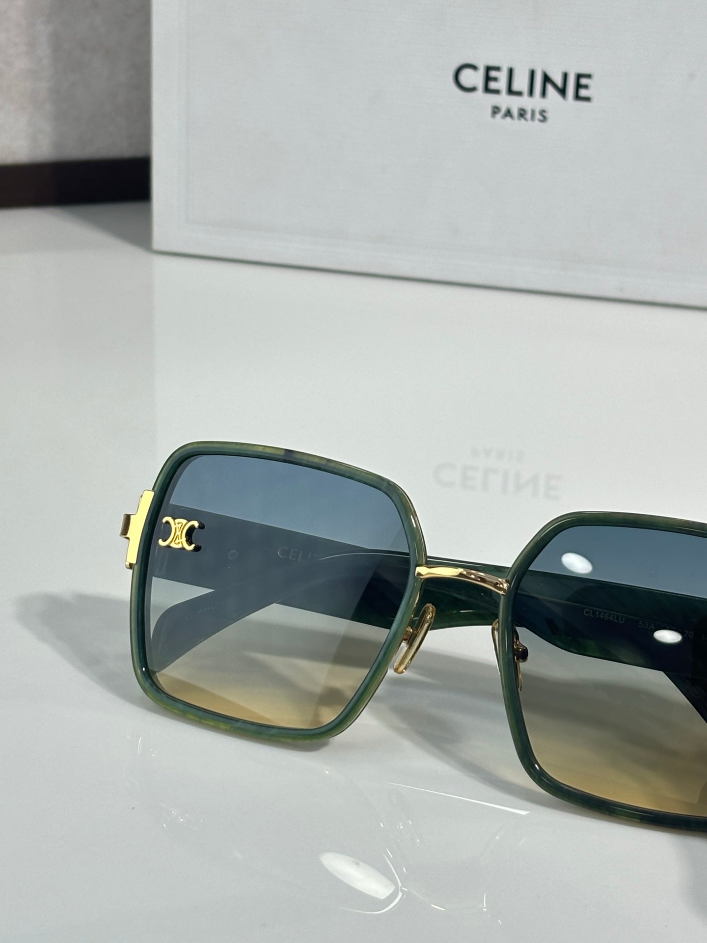 Celine sunglasses close-up with dark green frames and blue-tinted lenses, gold logo