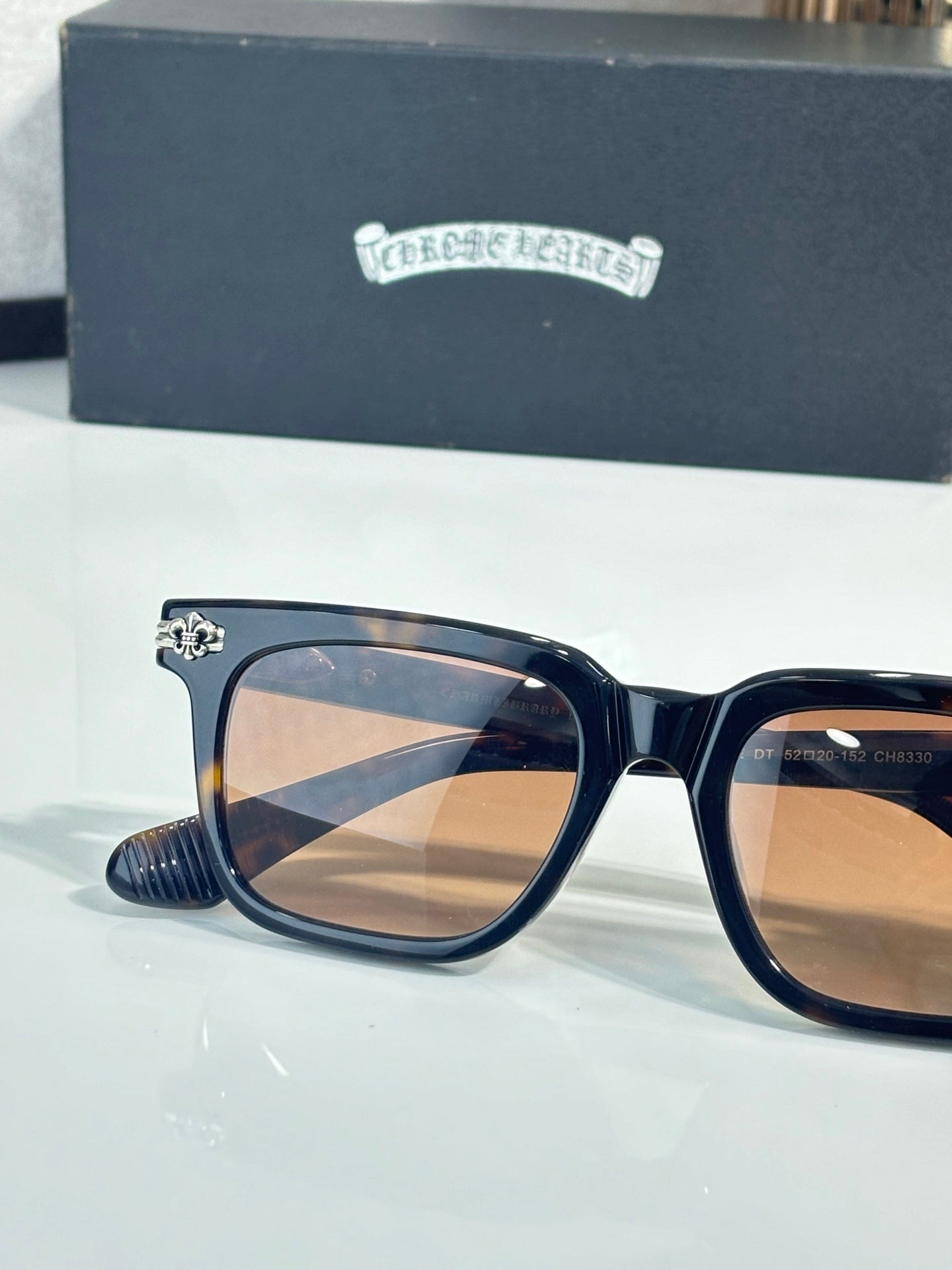Chrome glasses with dark blue frame, amber lenses, gold emblem on temple
