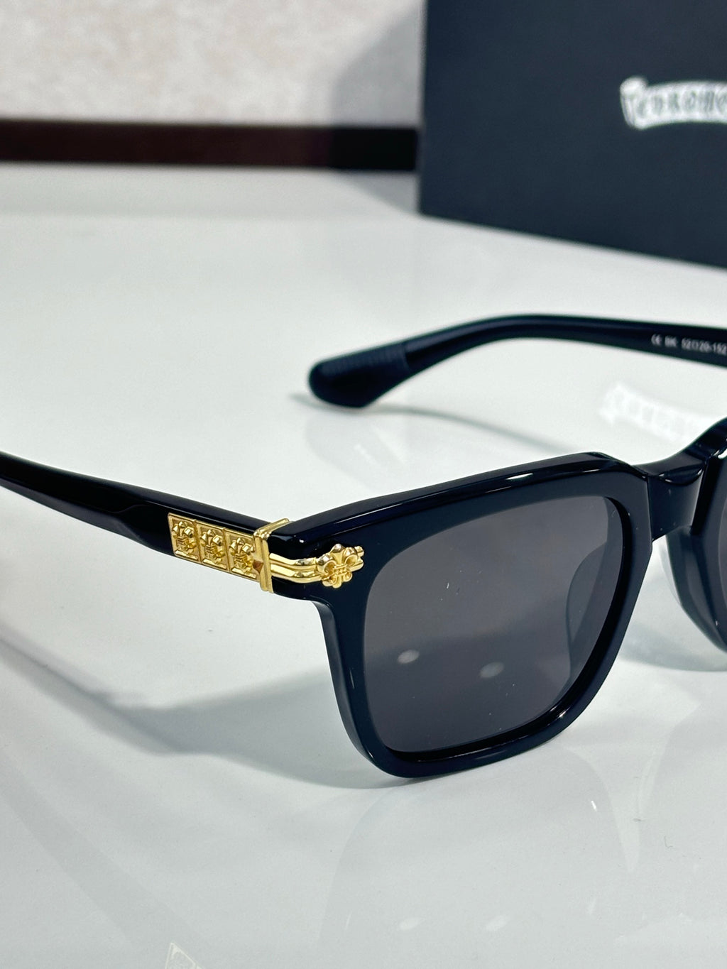 Chrome glasses with black frame, dark lenses, gold medallion detail on bridge