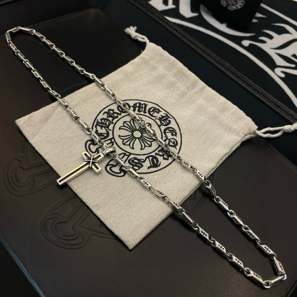 Cross pendant necklace draped over a light fabric pouch with ornate logo