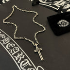 Silver-tone chain necklace with small cross pendant laid on dark surface