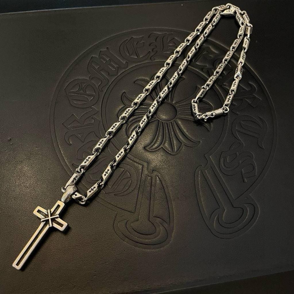 Silver-tone chain necklace with cross and sword-shaped pendant, close-up on black surface