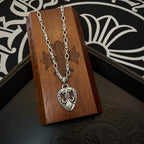 Silver chain necklace with heart crest pendant, resting on a small wooden box