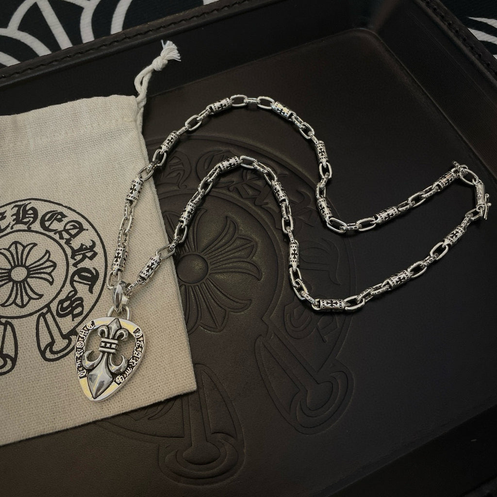 Silver chain necklace with heart crest pendant, shown in a light drawstring pouch