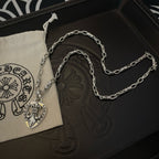 Silver chain necklace with heart crest pendant, shown in a light drawstring pouch
