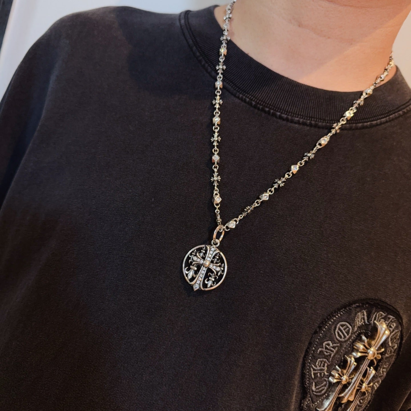 Silver-toned oval pendant necklace on long chain worn on dark T-shirt