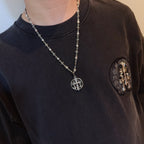 Silver-toned long necklace with oval crest pendant worn on dark crewneck