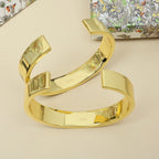 Stacked gold-tone cuff bracelets with engraved details and polished finish