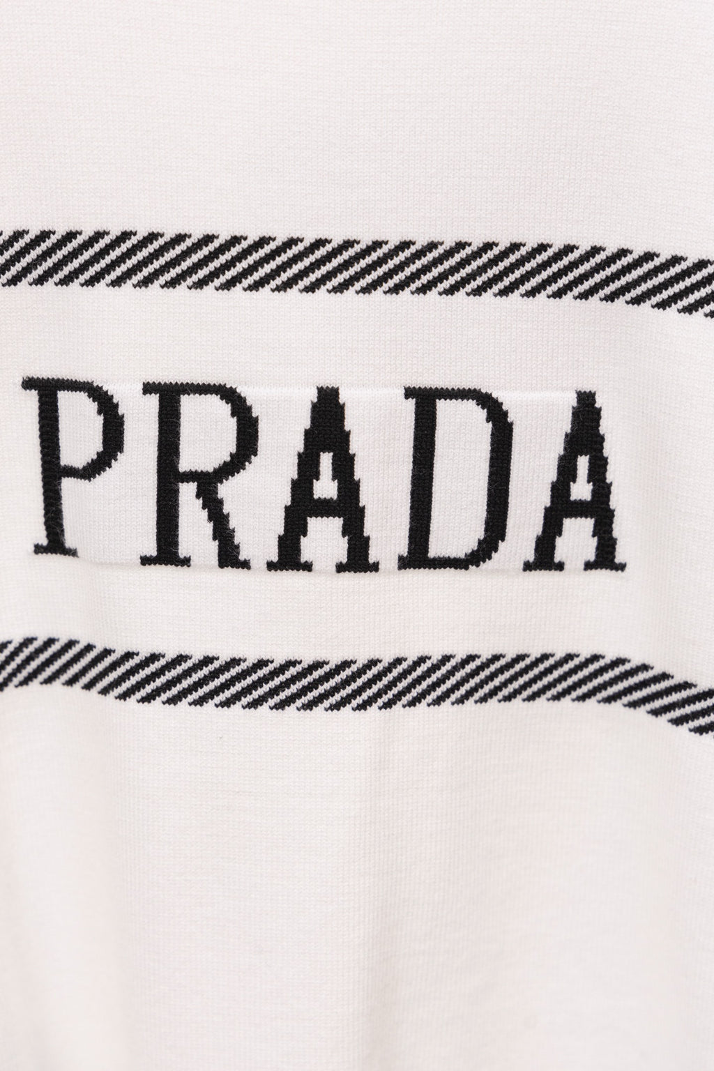 Close-up of white sweater with PRADA lettering and black striped detail
