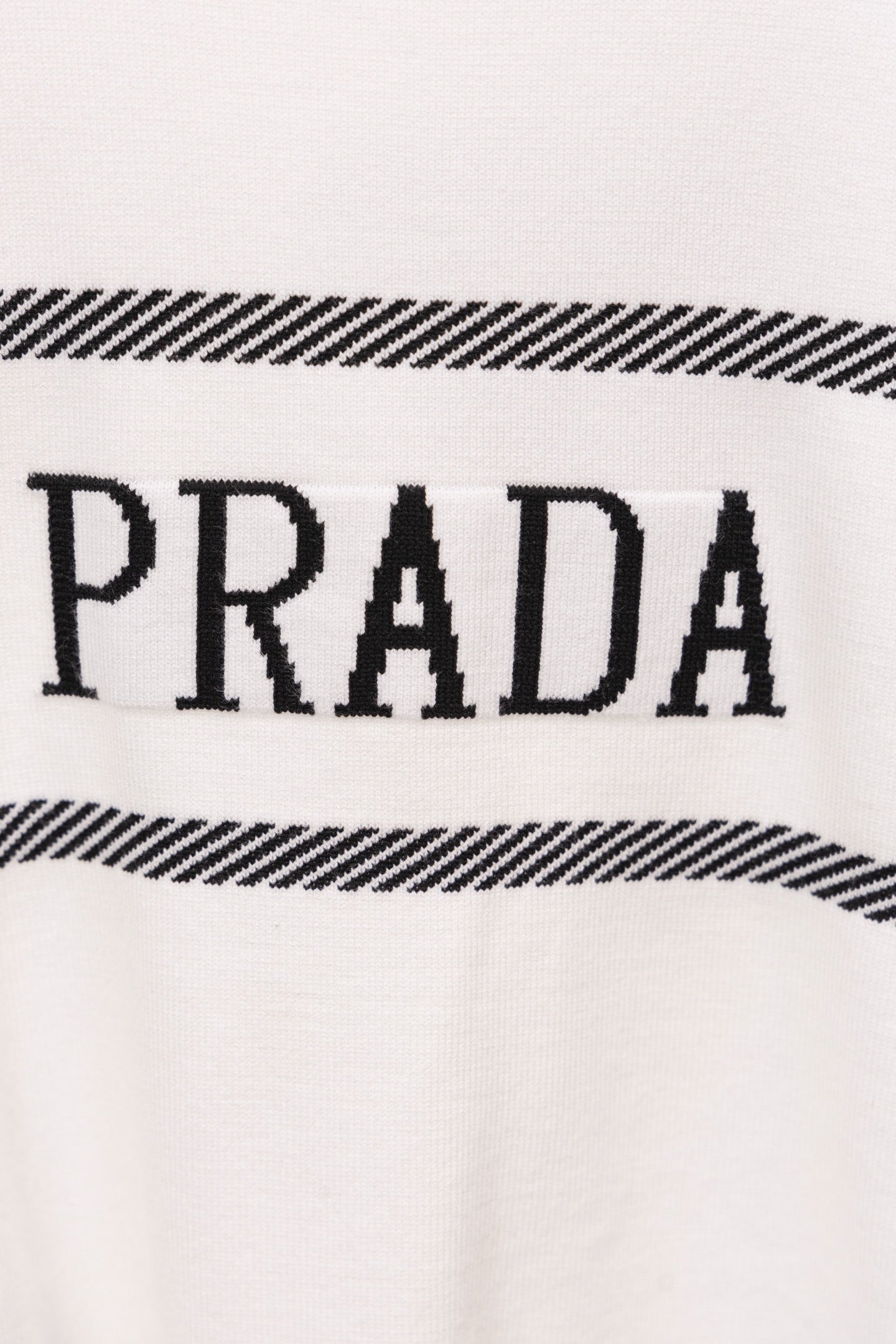 Close-up of white sweater with PRADA lettering and black striped detail