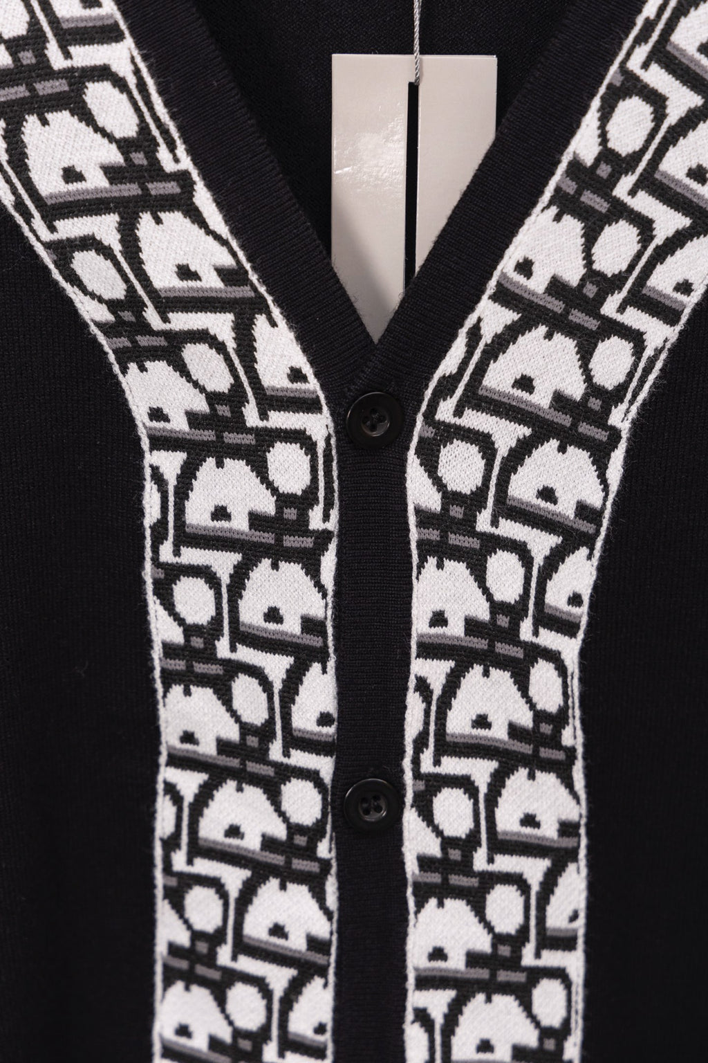 Close-up of black V-neck sweater with white patterned trim and two buttons