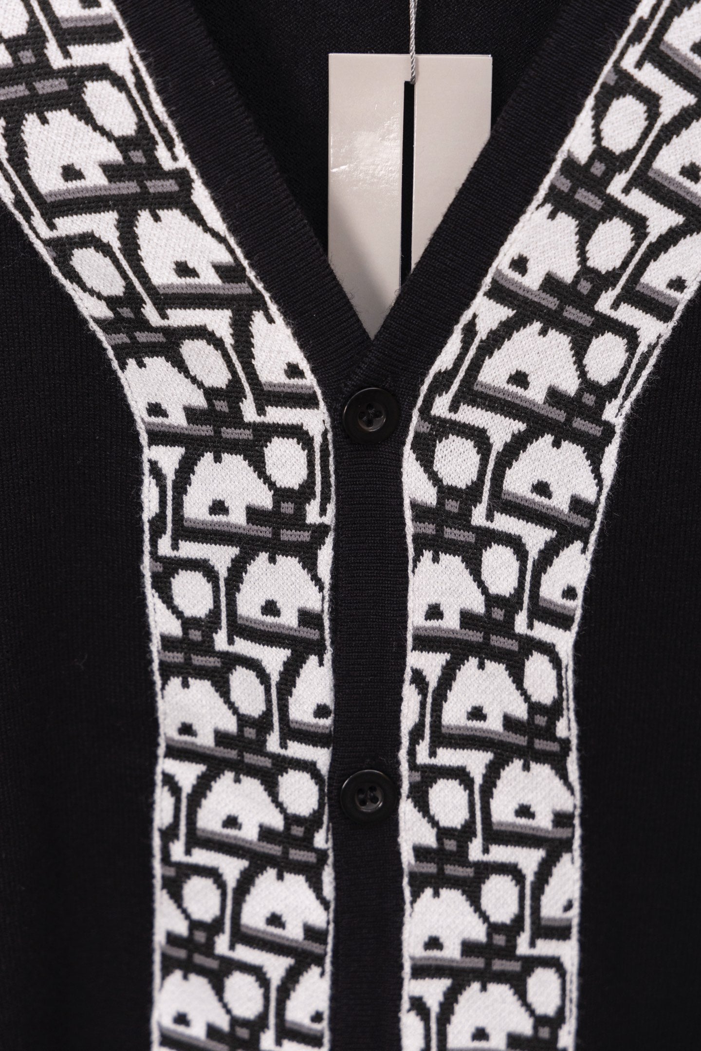 Close-up of black V-neck sweater with white patterned trim and two buttons